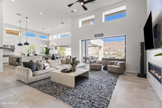 living room featuring ceiling fan, light tile patterned floors, a fireplace, a towering ceiling, and sink