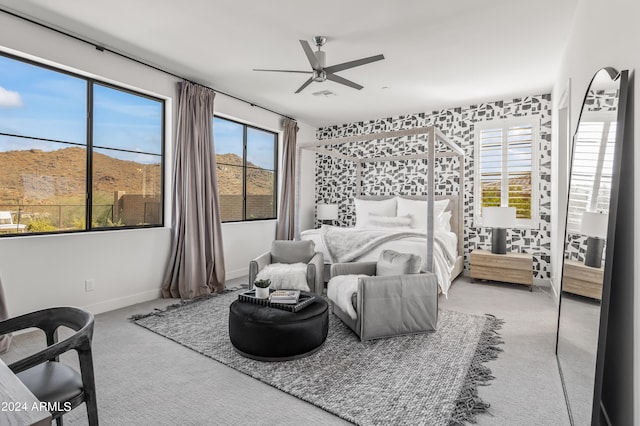 bedroom featuring a mountain view, multiple windows, light colored carpet, and ceiling fan