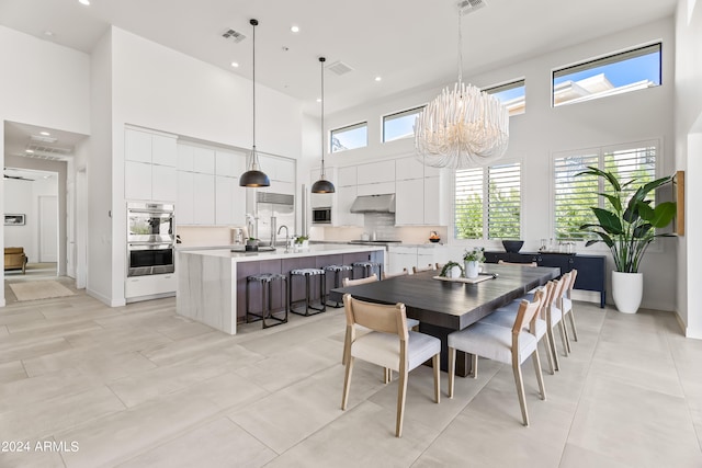 tiled dining space featuring a notable chandelier, a high ceiling, and a wealth of natural light