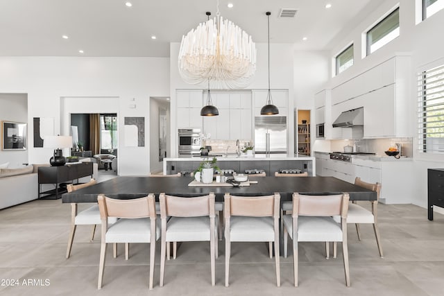 kitchen featuring wall chimney exhaust hood, hanging light fixtures, stainless steel appliances, an inviting chandelier, and a towering ceiling