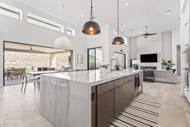 kitchen with a high ceiling, an island with sink, sink, light tile patterned flooring, and decorative light fixtures