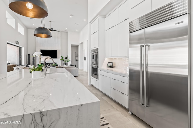 kitchen featuring white cabinets, light stone counters, sink, pendant lighting, and stainless steel appliances