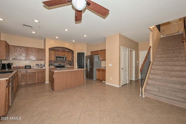 16112 W Durango St, Goodyear, AZ 85338 - kitchen featuring brown cabinets, stainless steel appliances, light tile patterned floors, tasteful backsplash, and a kitchen island