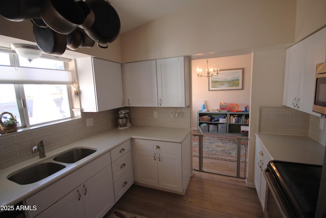 kitchen featuring a sink, electric range oven, a notable chandelier, and white cabinets