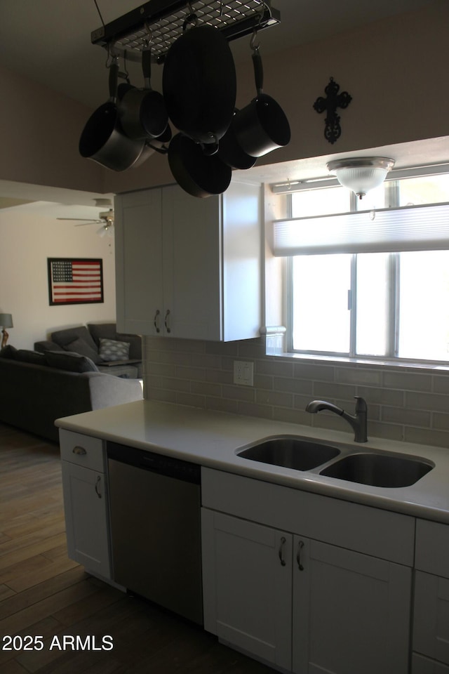 kitchen with backsplash, stainless steel dishwasher, a sink, light countertops, and dark wood-type flooring