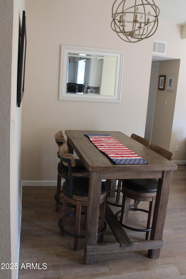 dining space featuring visible vents, baseboards, wood finished floors, and an inviting chandelier