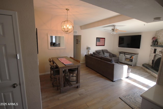 living area with a fireplace, ceiling fan with notable chandelier, baseboards, wood finished floors, and visible vents