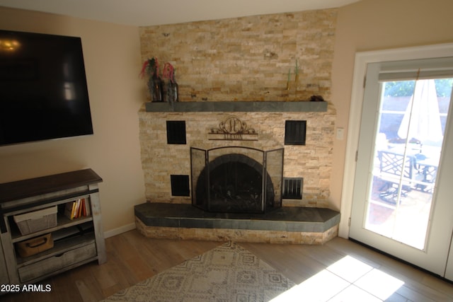 unfurnished living room featuring a stone fireplace, baseboards, wood finished floors, and visible vents