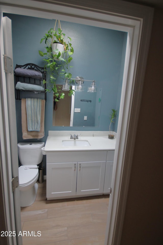half bath with vanity, toilet, and wood finished floors