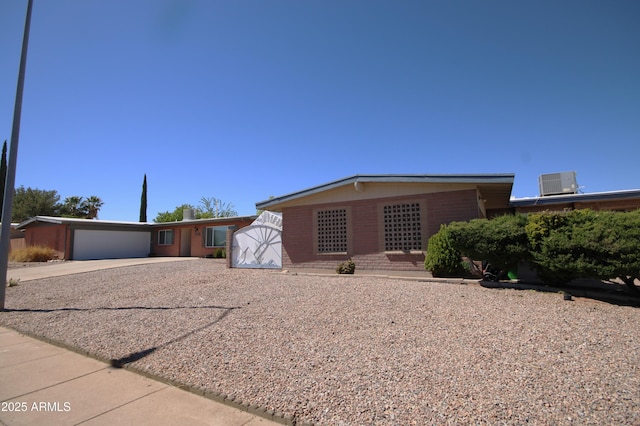 ranch-style home featuring a garage, cooling unit, driveway, and brick siding