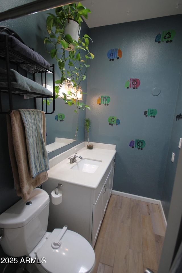 bathroom featuring vanity, baseboards, wood finished floors, and toilet
