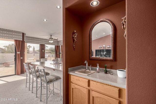 bar with light brown cabinets, light colored carpet, ceiling fan, and sink