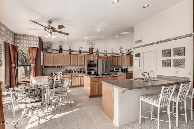 kitchen with a kitchen bar, stainless steel appliances, ceiling fan, sink, and a center island