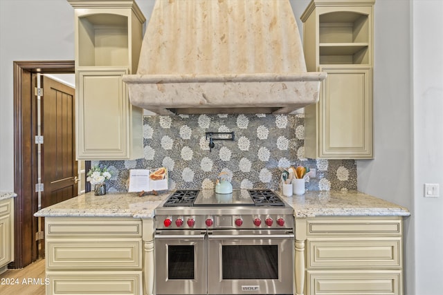 kitchen featuring range with two ovens, ventilation hood, cream cabinets, and tasteful backsplash