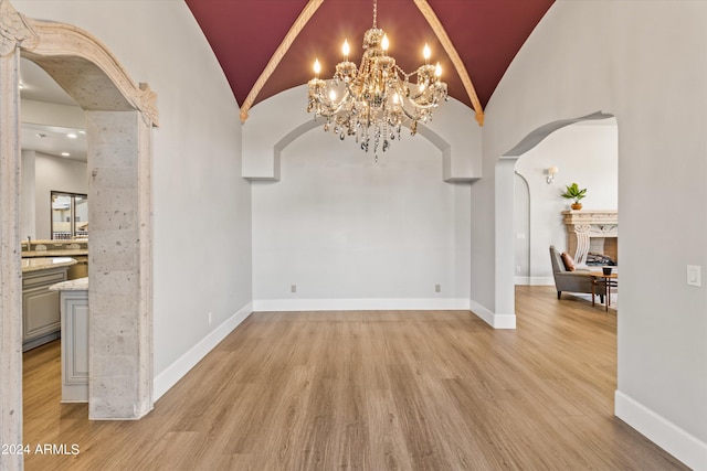 unfurnished dining area featuring arched walkways, lofted ceiling, light wood-style flooring, and baseboards