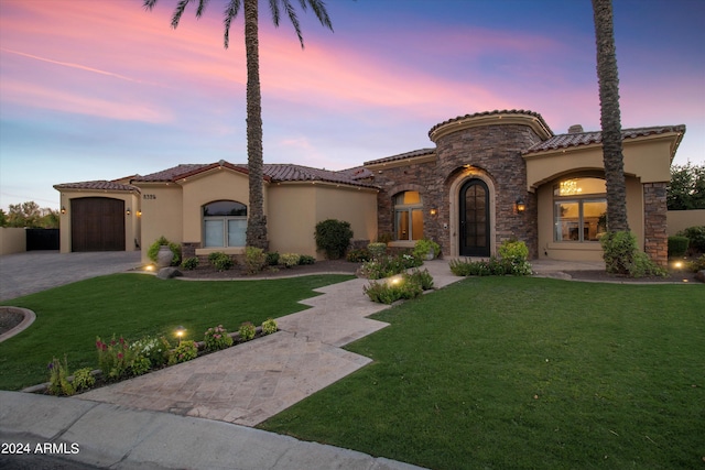 mediterranean / spanish home featuring a garage, stone siding, decorative driveway, stucco siding, and a front lawn