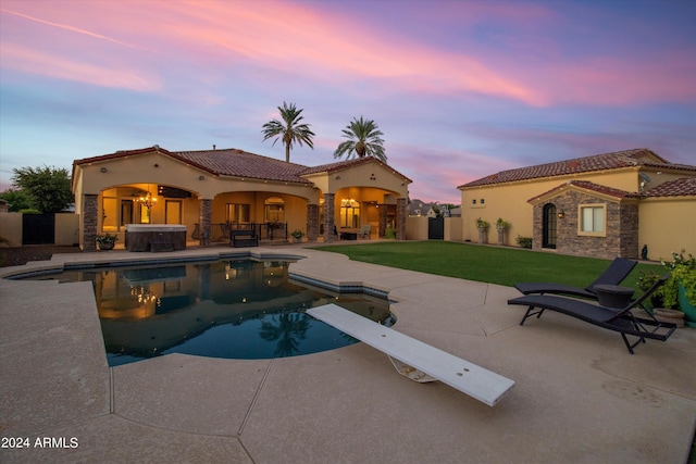 pool at dusk with a jacuzzi, a diving board, a yard, an outdoor pool, and a patio area