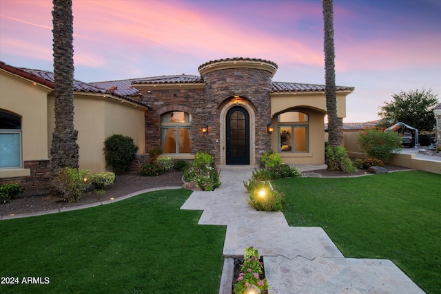 mediterranean / spanish home with stone siding, a lawn, a tile roof, and stucco siding