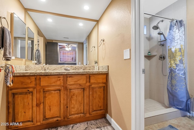 full bath featuring a tile shower, a sink, ceiling fan, and double vanity