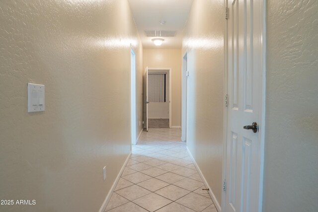 hallway with baseboards, light tile patterned flooring, and a textured wall