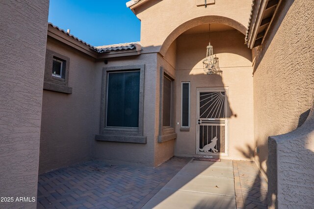 entrance to property with stucco siding, a tiled roof, and a patio area