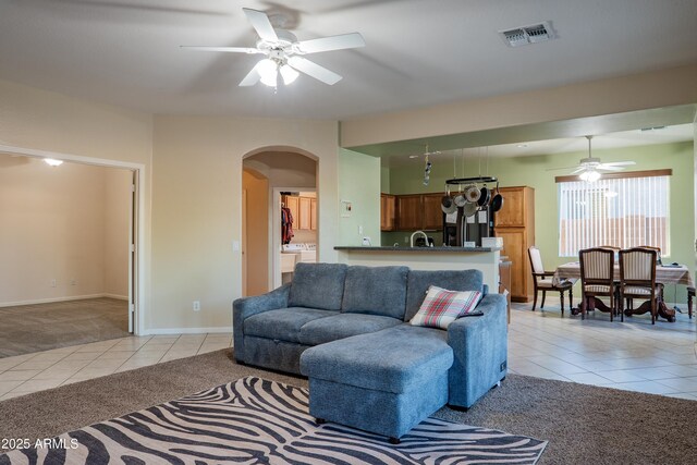living area featuring light tile patterned flooring, a ceiling fan, visible vents, light carpet, and arched walkways