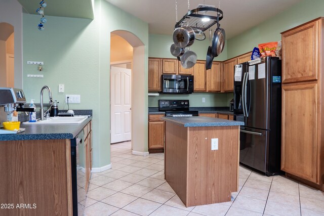 kitchen with a sink, a center island, dark countertops, arched walkways, and appliances with stainless steel finishes