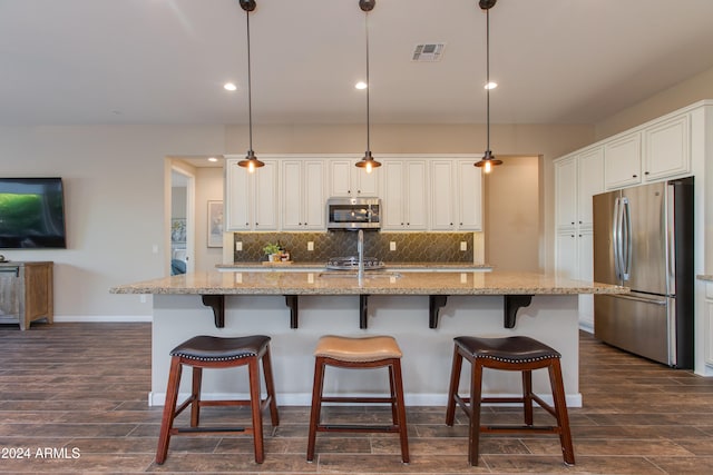 kitchen with dark hardwood / wood-style flooring, appliances with stainless steel finishes, hanging light fixtures, and an island with sink