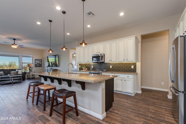 kitchen with light stone countertops, appliances with stainless steel finishes, white cabinetry, pendant lighting, and dark hardwood / wood-style floors