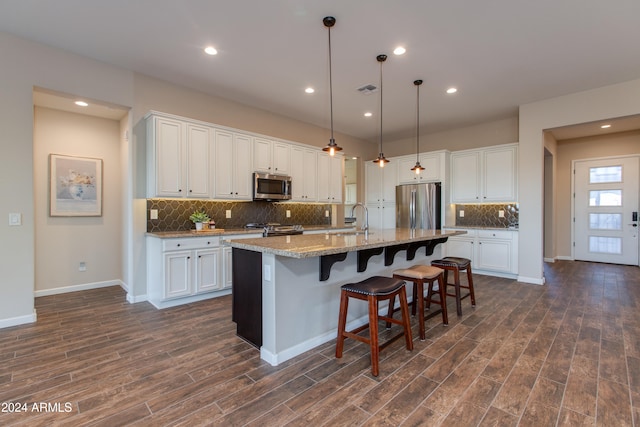 kitchen with light stone counters, dark hardwood / wood-style flooring, white cabinetry, a kitchen island with sink, and stainless steel appliances