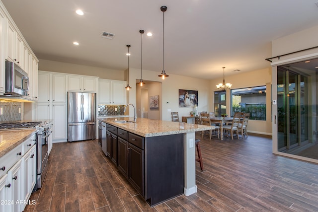 kitchen with dark hardwood / wood-style flooring, appliances with stainless steel finishes, backsplash, and an island with sink