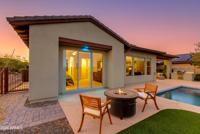 back house at dusk featuring an outdoor fire pit, a patio, and a fenced in pool