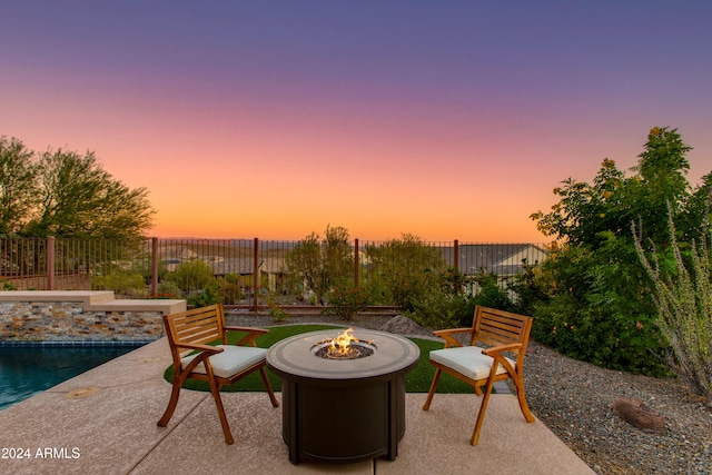 patio terrace at dusk with an outdoor fire pit and a fenced in pool