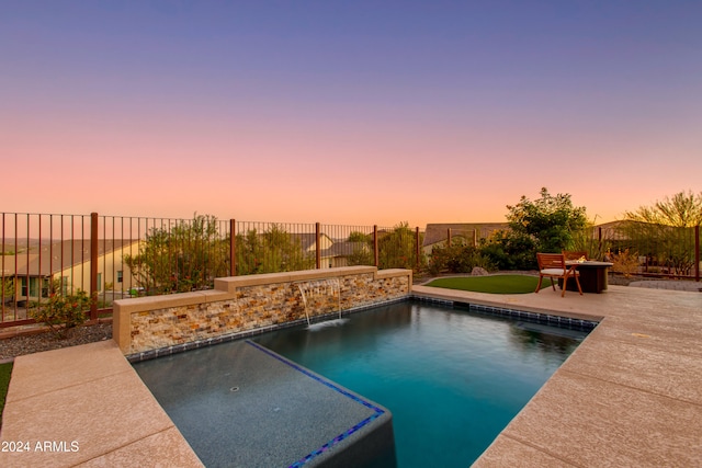 pool at dusk featuring pool water feature and a patio area