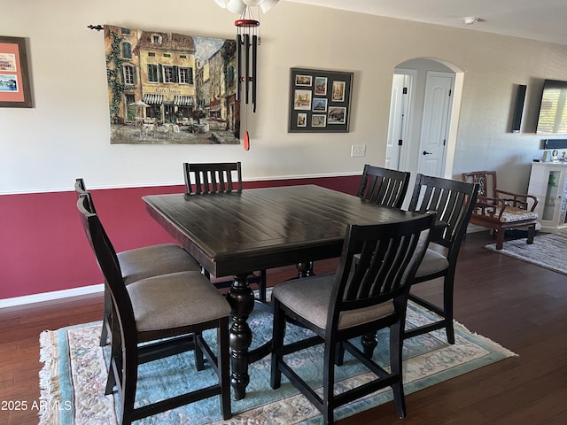 dining area with baseboards, arched walkways, and wood finished floors