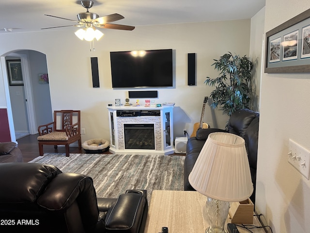 living area with wood finished floors, baseboards, a ceiling fan, a fireplace, and arched walkways