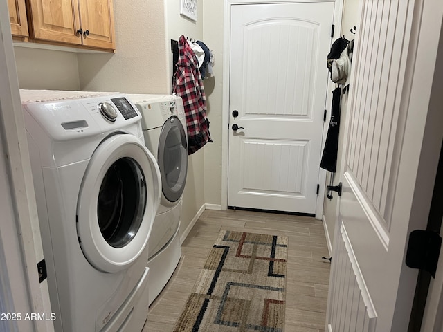 washroom with baseboards, wood finish floors, washer and clothes dryer, a textured wall, and cabinet space