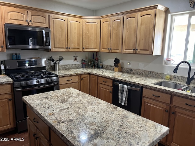 kitchen with light stone countertops, appliances with stainless steel finishes, a kitchen island, and a sink