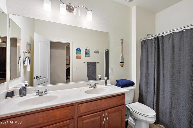 bathroom featuring a shower with shower curtain, toilet, double vanity, and a sink