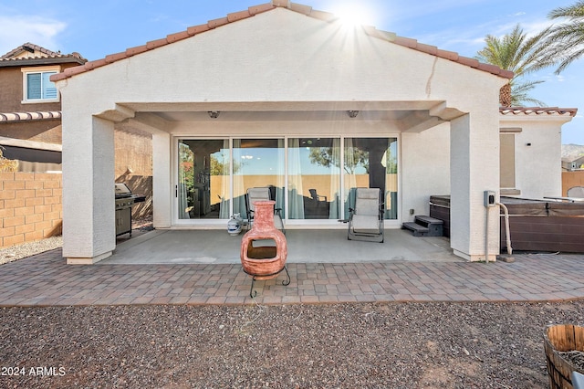 back of house featuring stucco siding, a tile roof, a patio, and a hot tub