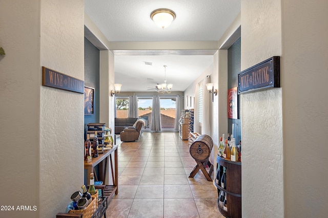 corridor featuring light tile patterned flooring, an inviting chandelier, a textured wall, and visible vents