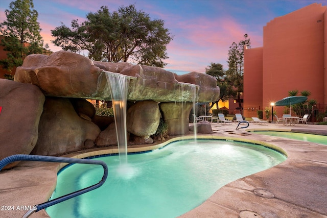 pool at dusk with pool water feature and a patio