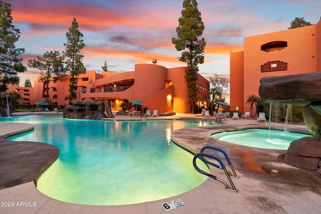 pool at dusk with pool water feature, a patio area, and a hot tub