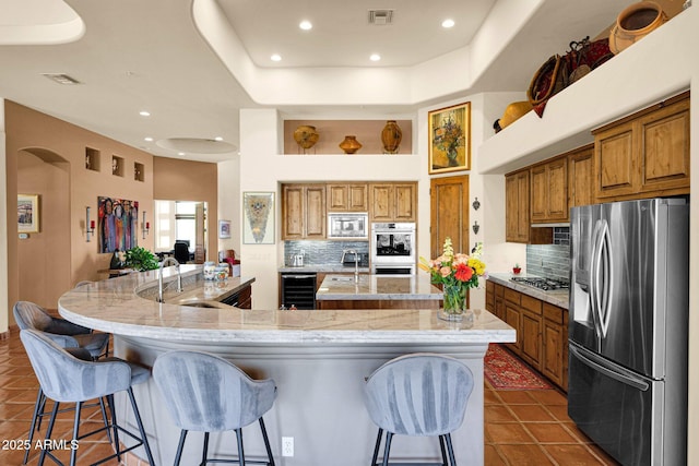 8154 E Tecolote Cir, Scottsdale, AZ 85266 - kitchen featuring appliances with stainless steel finishes, wine cooler, a large island with sink, brown cabinetry, and recessed lighting