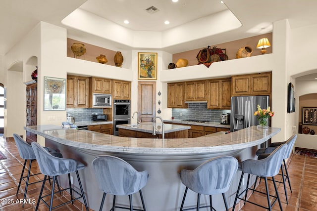 8154 E Tecolote Cir, Scottsdale, AZ 85266 - kitchen with stainless steel appliances, brown cabinetry, a towering ceiling, decorative backsplash, and arched walkways