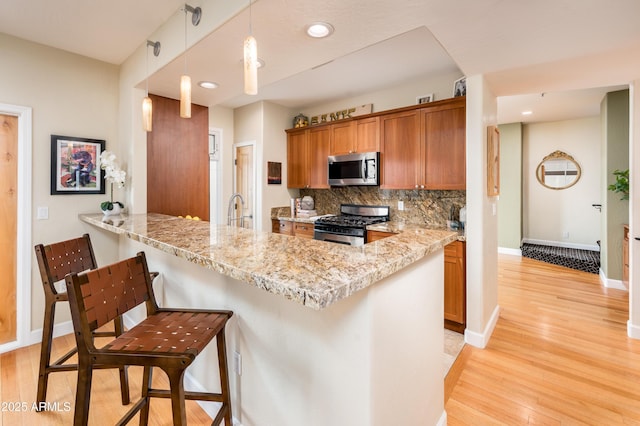 kitchen with tasteful backsplash, decorative light fixtures, light hardwood / wood-style flooring, appliances with stainless steel finishes, and kitchen peninsula