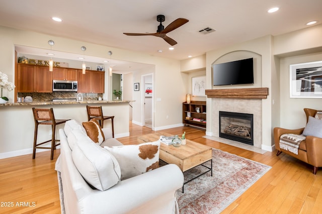 living room featuring ceiling fan, light hardwood / wood-style floors, and a tile fireplace