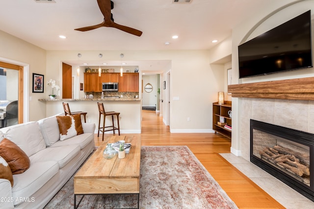 living room featuring a tile fireplace, light wood-type flooring, and ceiling fan