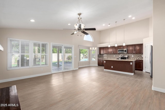 kitchen with appliances with stainless steel finishes, a kitchen island with sink, ceiling fan, decorative light fixtures, and high vaulted ceiling