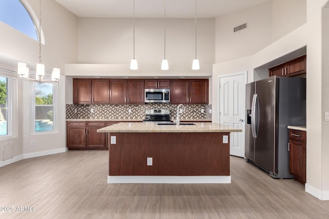 kitchen featuring decorative light fixtures, a towering ceiling, an island with sink, and appliances with stainless steel finishes